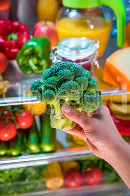 Woman takes the broccoli from the open refrigerator.