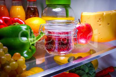 Fresh raspberries in a glass jar on a shelf open refrigerator