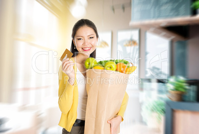 Asian woman holding groceries bag and credit card in market