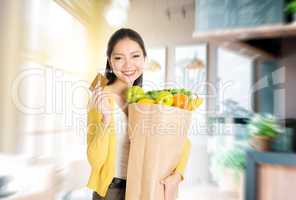 Asian woman holding groceries bag and credit card in market