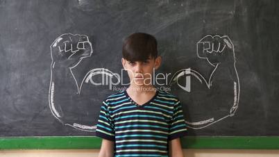 Strong Male Child Showing Muscles In Classroom At Lesson