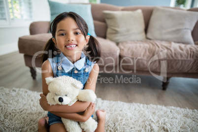 Portrait of girl with teddy bear sitting in living room