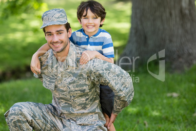 Portrait of army soldier giving piggyback ride to boy in park