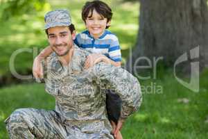 Portrait of army soldier giving piggyback ride to boy in park