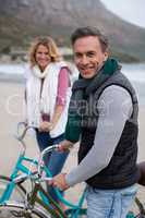 Mature couple standing with bicycles on the beach