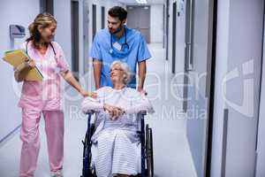 Male and female doctor interacting with female senior patient on wheelchair in corridor