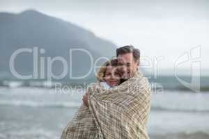 Mature couple wrapped in blanket on the beach