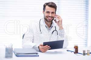 Male doctor talking on mobile phone while using digital tablet
