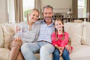 Portrait of smiling parents and daughter sitting on sofa in living room