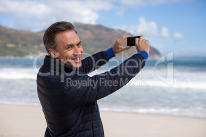 Mature man photographing scenery using cell phone on the beach
