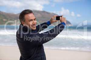 Mature man photographing scenery using cell phone on the beach