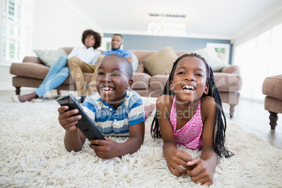 Siblings lying on rug and watching television in living room