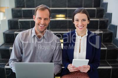 Businessman and woman sitting on steps holding laptop