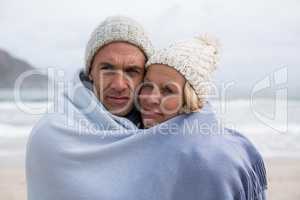 Mature couple wrapped in blanket on the beach