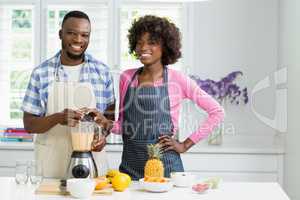 Smiling couple preparing strawberry smoothie in kitchen at home