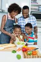 Parents and kids preparing salad in kitchen