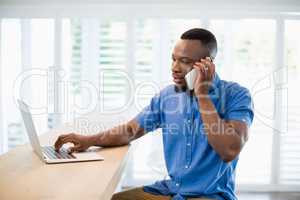 Man talking on phone while using laptop in living room