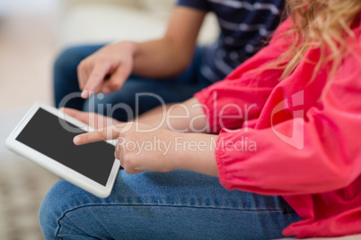 Siblings using digital tablet on sofa in living room