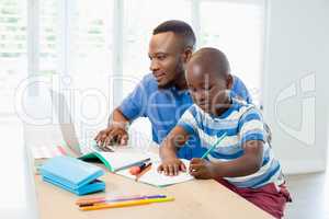 Father using laptop and son doing his homework in living room