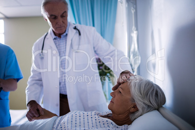 Doctors comforting senior patient on bed