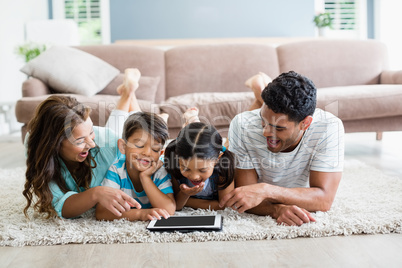 Parents and children lying on rug and using digital tablet in living room