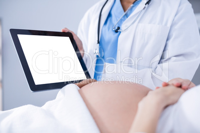 Doctor showing ultrasound scan on to pregnant woman on digital tablet