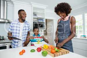 Mother and son preparing salad while father using digital tablet in kitchen