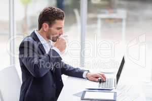 Businessman using laptop at desk and drinking coffee