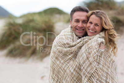 Mature couple wrapped in blanket on the beach