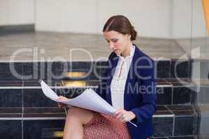 Businesswoman sitting on steps holding blueprint