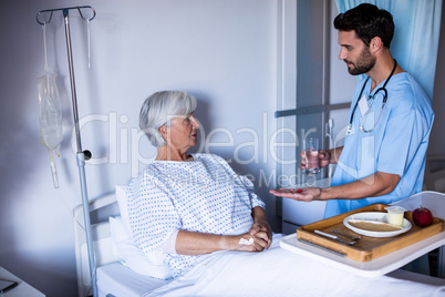 Doctor serving medicine to female senior patient on bed