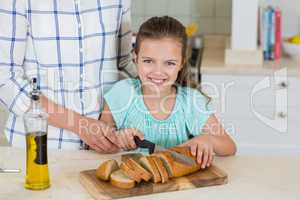Mother assisting a daughter to slice the loaf bread