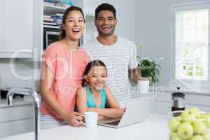 Parents and daughter using laptop while having coffee in kitchen at home