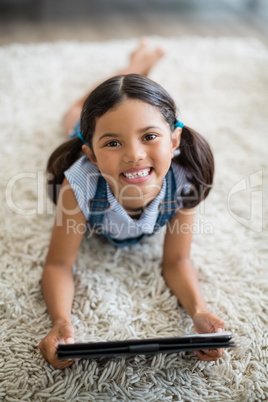 Girl using digital tablet while lying on rug in living room at home