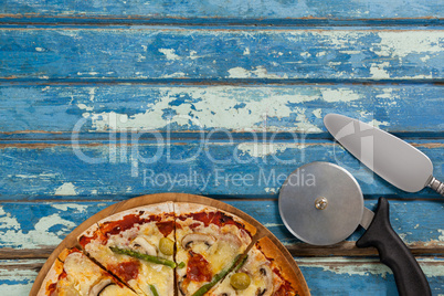 Italian pizza served on pizza tray with cutter and knife on wooden plank