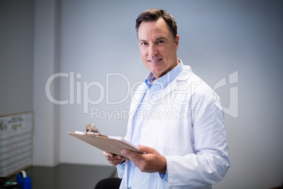 Portrait of male doctor holding clipboard in corridor