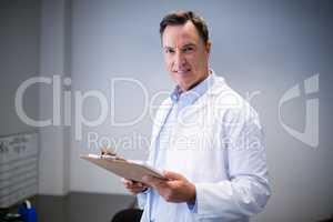 Portrait of male doctor holding clipboard in corridor