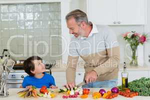 Father interacting with son while slicing a cucumber on chopping board in kitchen