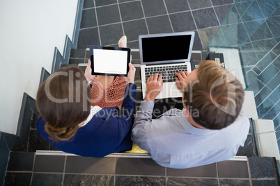 Businessman and woman sitting on steps using laptop and digital tablet