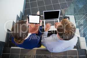 Businessman and woman sitting on steps using laptop and digital tablet