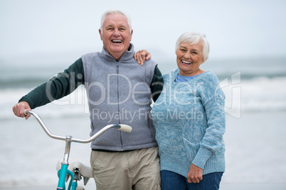 Senior couple standing with bicycle on the beach