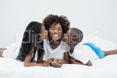 Mother receiving kiss from their kids in bedroom