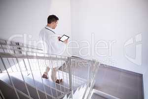 Doctor using digital tablet while walking down staircase