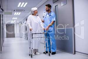 Male doctor assisting senior patient to walk with her walker