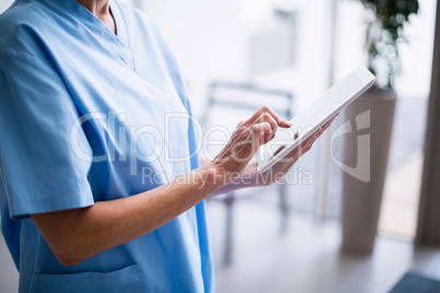 Nurse standing in hospital corridor using digital tablet