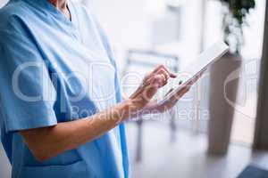 Nurse standing in hospital corridor using digital tablet