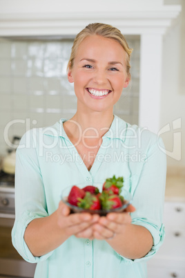 Beautiful woman holding glass of strawberry in kitchen