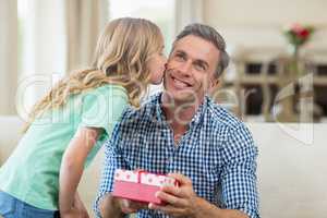 Girl kissing her father on cheek in living room