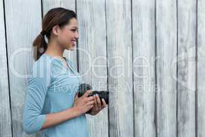 Happy female photographer standing against wooden background