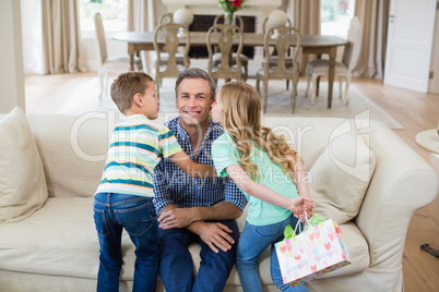 Son and daughter kissing their father on cheek in living room